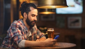 people and technology concept - happy man with smartphone drinking beer and reading message at bar or pub