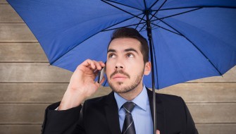 Serious businessman under umbrella phoning against wooden surface with planks
